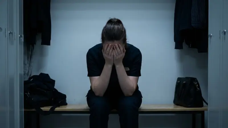 薄暗い空間に座り込み手で顔を覆っている女性。